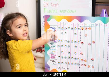 Tableau de motivation des tâches pour une fille de quatre ans, elle pointe sur le tableau et parle de tâche Banque D'Images