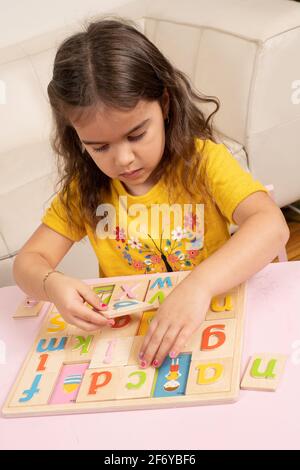 Fille de quatre ans jouant avec un puzzle en bois alphabet, mettant des lettres colorées dans leurs taches Banque D'Images