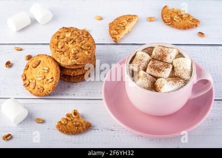 Café avec guimauves et biscuits sur une table en bois blanc. La nourriture. Tasse à latte rose et soucoupe sur planches de bois. Composition rustique, boisson chaude Banque D'Images