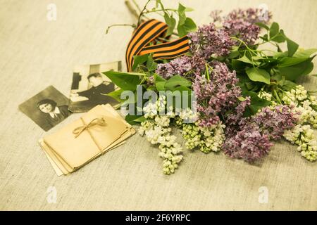 Jour de la victoire. Nous nous souvenons des exploits de nos grands-pères. Ruban de Saint-George, lettres de guerre, photographies sur le fond de lilas en fleurs. Banque D'Images