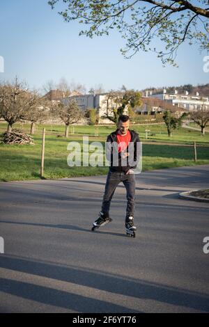 Jeune homme sur la lame de rouleau regardant son téléphone. Technologie dans la nature. Banque D'Images