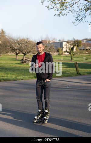 Jeune homme sur la lame de rouleau regardant son téléphone. Technologie dans la nature. Banque D'Images