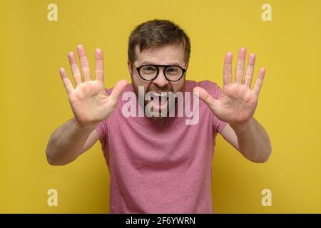 Heureux, hurlant homme en lunettes montre le numéro dix avec ses doigts, deux paumes ouvertes. Signe 10 émotions positives. Arrière-plan jaune. Banque D'Images