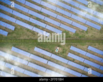 Le soleil se lève au-dessus de la baie de panneaux solaires ferme en rangées sur le champ ensoleillé. Production d'électricité renouvelable verte avec lumière du soleil vue aérienne drone Banque D'Images