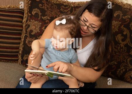 bébé fille de 7 mois lu par la mère, bby pointant vers le livre Banque D'Images