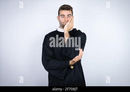 Jeune homme hispanique portant l'uniforme d'un prêtre debout sur fond blanc penser en train de regarder fatigué et s'ennuyer avec des bras croisés Banque D'Images