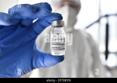 Une infirmière en combinaison et gants d'epi tient la simulation Astra Zeneca vaccin devant la caméra Banque D'Images