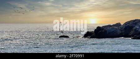 Silhouette d'une personne pratiquant la planche à voile dans une mer calme au coucher du soleil Banque D'Images