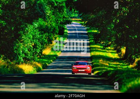 La conduite d'une voiture de sport Jaguar le long de la route de campagne a été accompagnée de réglages lumière du soleil Banque D'Images