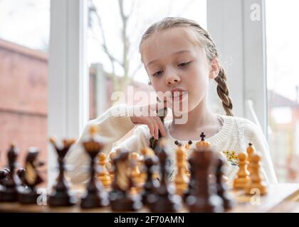 Belle mignonne génie enfant jeune fille jouant aux échecs avec des pièces sur l'échiquier, un gamin se concentre sur la reine du roi pour chéquier Banque D'Images