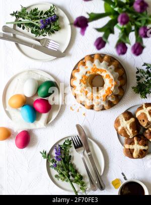 Petit-déjeuner de Pâques - table de cuisine avec œufs de pâques peints à la main, babka traditionnel de Pâques, pains à croix chaude, thé frais, tulipes. Banque D'Images