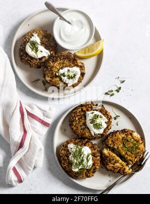 Dîner - beignets de quinoa et de courgettes cuites au four végétalien, servis sur des assiettes avec aneth, micro herbes et crème sure végétalienne, prêts à être mangés. Banque D'Images