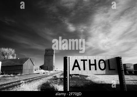 Le signe du marqueur ferroviaire fissuré pour Athol, Dakota du Sud, avec quelques structures agricoles en arrière-plan de l'image infrarouge noir et blanc. Banque D'Images