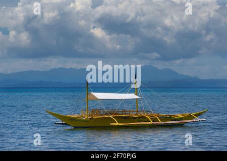 Un canot jaune en outrigger amarré au large de la côte dans la mer de Visayan. Île Malapascua, Cebu, Philippines. Banque D'Images