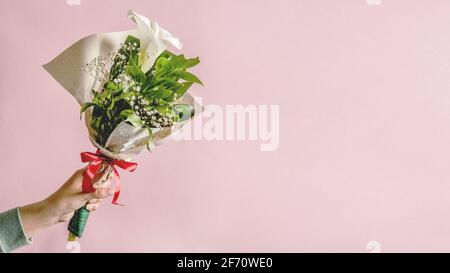 Mains de femme caucasienne inconnue tenant un bouquet de Calla décoré Fleur de Zantedeschia devant un fond ou un mur rose - félicitations Banque D'Images