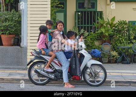 Une mère avec ses trois enfants sur une moto, un des garçons absorbé dans son téléphone mobile; Phuket Town, Thaïlande, Asie du Sud-est Banque D'Images