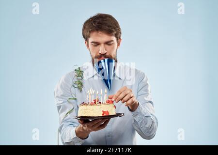 Homme barbu avec une assiette de gâteau sur un bleu arrière-plan et un chapeau de fête d'anniversaire sur sa tête Banque D'Images