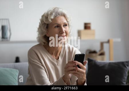 Bonne femme mûre pensive tenant un smartphone à la maison Banque D'Images