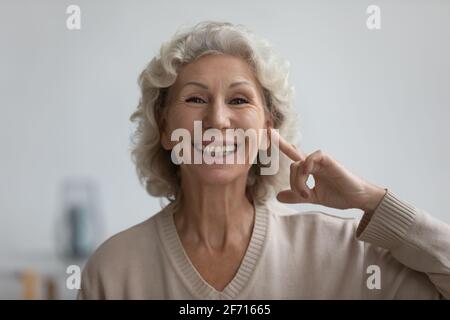 Portrait d'une femme âgée heureuse pointant du doigt vers l'oreille Banque D'Images