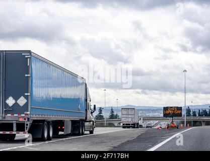 Convoi de gros engins semi-camions industriels transportant des marchandises semi-remorques de camionnettes sèches roulant dans la file sur le large intersection avec différents Banque D'Images