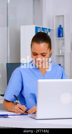 L'infirmière prend des notes sur le presse-papiers après avoir lu les viols médicaux du patient à partir d'un ordinateur portable. Médecin de santé en uniforme, médecin assistant travaillant dans l'hôpital vérifiant l'enregistrement, écrivant les traitements Banque D'Images