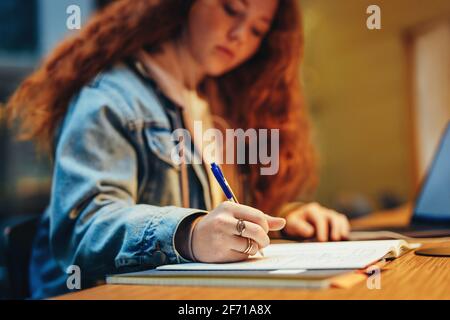 Gros plan d'une adolescente prenant des notes dans la bibliothèque. Une étudiante étudie tard dans la nuit à la bibliothèque de l'université. Banque D'Images