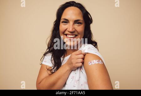 Portrait d'une femme souriant après avoir reçu un vaccin. Femme tenant sa manche et montrant son bras avec un bandage après avoir reçu la vaccination. Banque D'Images