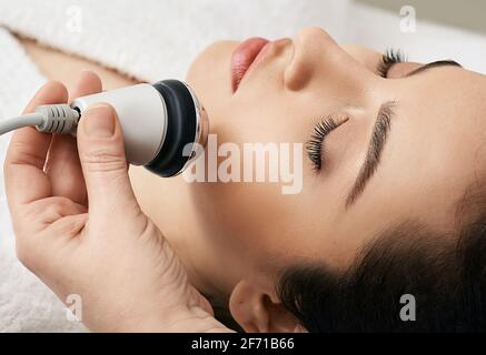 Brunette femme recevant une procédure de levage par radiofréquence pour sa peau de visage rajeunissement à la clinique de cosmétologie esthétique Banque D'Images