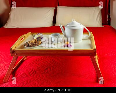 Un petit-déjeuner est servi sur un plateau en bois avec des pliages jambes sur un lit rouge Banque D'Images