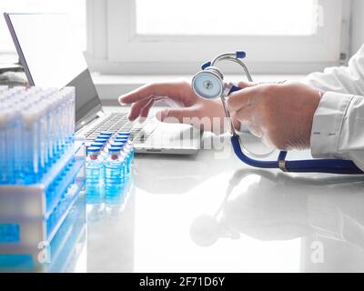 Vaccination concept de recherche médicale. Mains d'un médecin travaillant à un ordinateur portable. Il remplit le questionnaire du patient en ligne. Banque D'Images