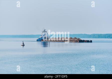 le remorqueur pousse la barge de cargaison en vrac sèche avec du sable sur le rivière dans la brume matinale Banque D'Images