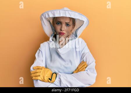 Belle blonde blanche femme portant l'uniforme de gardien de beekeeper protecteur sceptique et nerveux, désapprouvant l'expression sur le visage avec les bras croisés. Négatif Banque D'Images