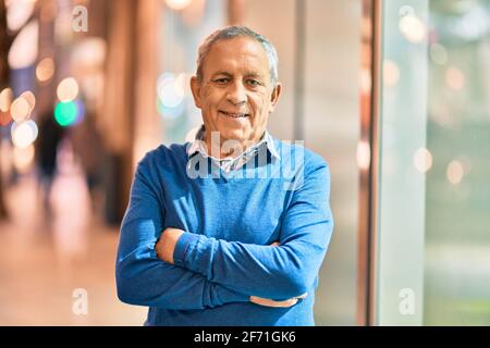 Homme âgé aux cheveux gris avec les bras croisés souriant heureux debout dans la ville. Banque D'Images