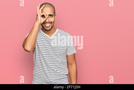 Homme hispanique adulte portant des vêtements décontractés faisant geste ok avec la main souriant, oeil regardant à travers les doigts avec le visage heureux. Banque D'Images