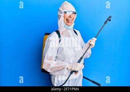 Jeune fille blonde portant l'équipement Covid-19 collant la langue dehors heureux avec l'expression drôle. Banque D'Images