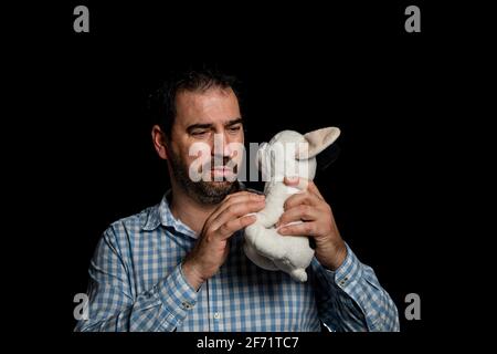 Homme barbu en chemise à carreaux bleu et blanc qui câblent un chiot bourré sur fond noir de studio. Concept de jeu Banque D'Images