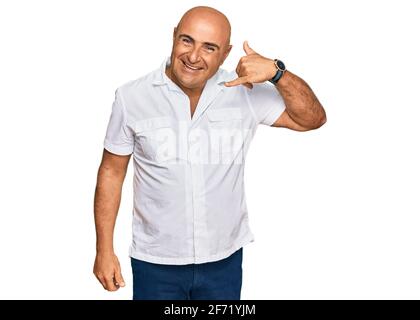 Homme mature du Moyen-Orient avec moustache portant une chemise blanche décontractée souriant faisant un geste de téléphone avec la main et les doigts comme parler au téléphone. commu Banque D'Images