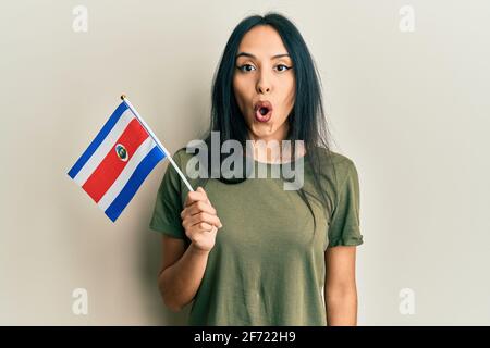 Jeune fille hispanique portant le drapeau du costa rica effrayée et stupéfait avec la bouche ouverte pour la surprise, le visage incrédulé Banque D'Images