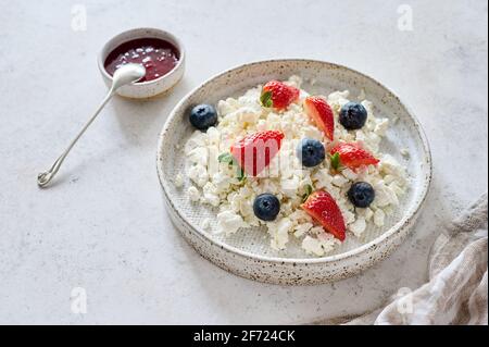 Fromage cottage avec bleuets et fraises dans une assiette sur fond clair. Confiture de framboises à proximité avec cuillère. Concept petit déjeuner sain Banque D'Images