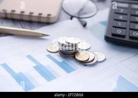pile de pièces, graphique financier, calculatrice et bloc-notes sur la table Banque D'Images
