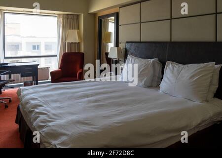 Chambre d'hôtel ou d'appartement moderne avec lit king-size fraîchement préparé et éclairage naturel depuis la fenêtre. Banque D'Images