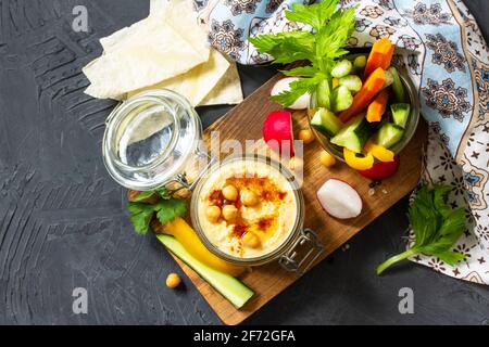 Cuisine arabe. Houmous du Moyen-Orient avec en-cas. Trempez le houmous avec des bâtonnets de légumes frais sur un comptoir en pierre foncée. Vue de dessus. Pose à plat. Banque D'Images