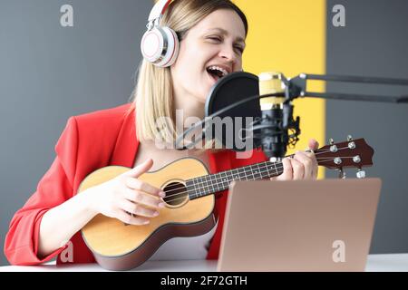 Femme chante et joue de la guitare avec des écouteurs devant microphone Banque D'Images