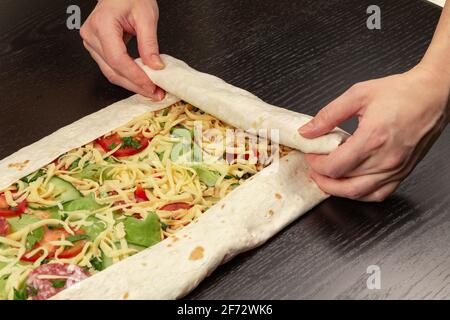 les mains des femmes enveloppent la salade de légumes frais avec du fromage dans du pain pita. la cuisson du shawarma sur une table en bois noir Banque D'Images