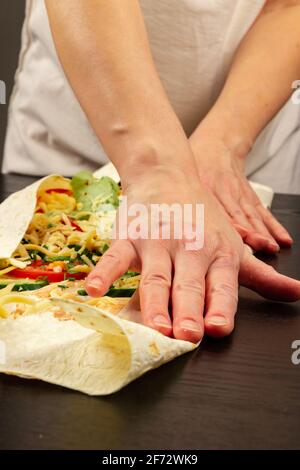 les mains des femmes enveloppent la salade de légumes frais avec du fromage dans du pain pita. la cuisson du shawarma sur une table en bois noir Banque D'Images