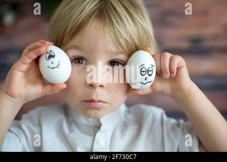 Mignon enfant, tenant des oeufs blancs avec des émotions tirées sur eux pour Pâques, visages drôles Banque D'Images