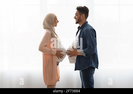 Femme enceinte islamique en hijab comparant la taille du ventre avec elle mari Banque D'Images