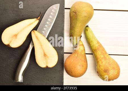 Trois poires de conférence entières et deux poires de conférence sucrées et sucrées et semi-biologiques et juteuses et un couteau en métal avec une assiette de service en ardoise, sur une table en bois naturel, Banque D'Images