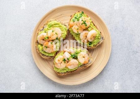 Toast à l'apéritif avec avocat et crevettes sur une assiette de bambou, vue sur la table. Isolé sur fond en béton gris. Avocat et bruschetta aux crevettes Banque D'Images