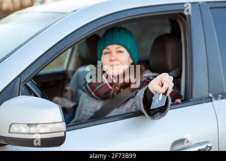 Femme un chauffeur qui effectue un paiement sans espèces par carte de crédit à l'intérieur de sa voiture, regardant la caméra Banque D'Images